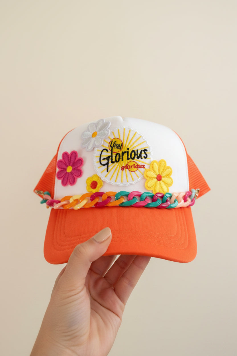 Orange and white cap with floral decorations and 'Glorious' logo on a surface.