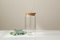 create an image of a 16 oz glass with a bamboo lid and clear straw. There is a small bit of greenery laying next to the glass