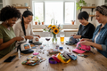 Create an image of four female adults around a kitchen island decorating trucker hats with iron on patches, gemstones, and ribbons. They are a diverse group and and table has a glass of wine and a pint of beer on the kitchen island. There is a small vase of flowers also on the kitchen island. 